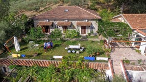 Una casa de piedra con techo de tejas, rodeada de vegetación y un paisaje montañoso.