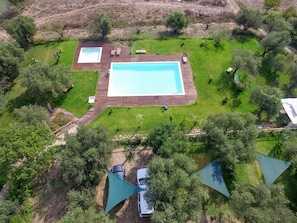 Ein Luftbild eines Anwesens mit einem rechteckigen Schwimmbecken, umgeben von einer Holzterrasse, einer Rasenfläche und Bäumen.