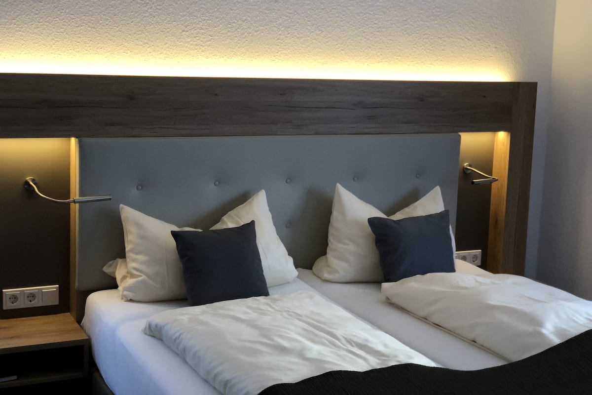 A neatly made bed with white and dark pillows, a wooden headboard, and bedside lamps.
