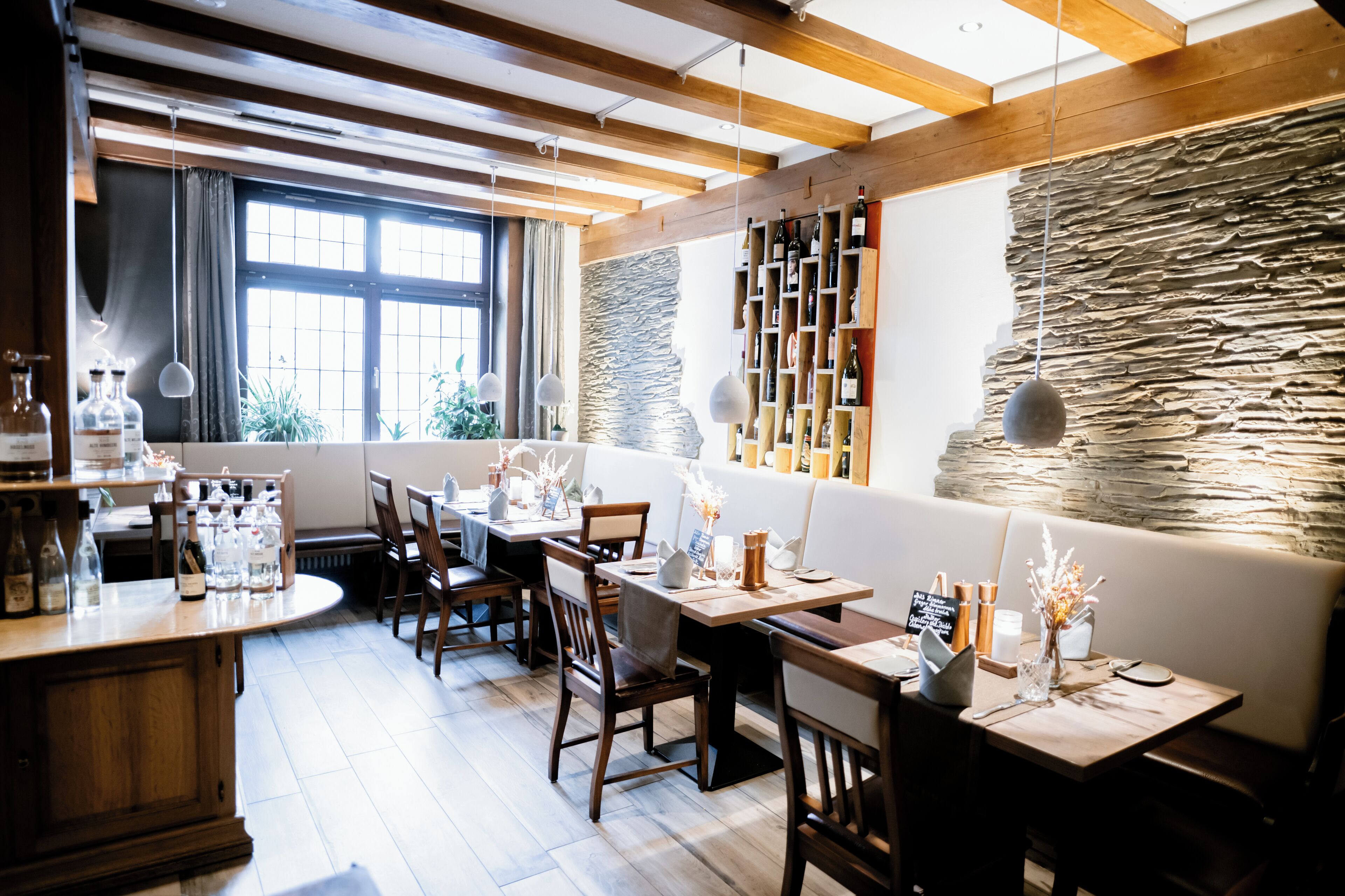 A restaurant with wooden beams, stone wall, and a variety of bottles on shelves.