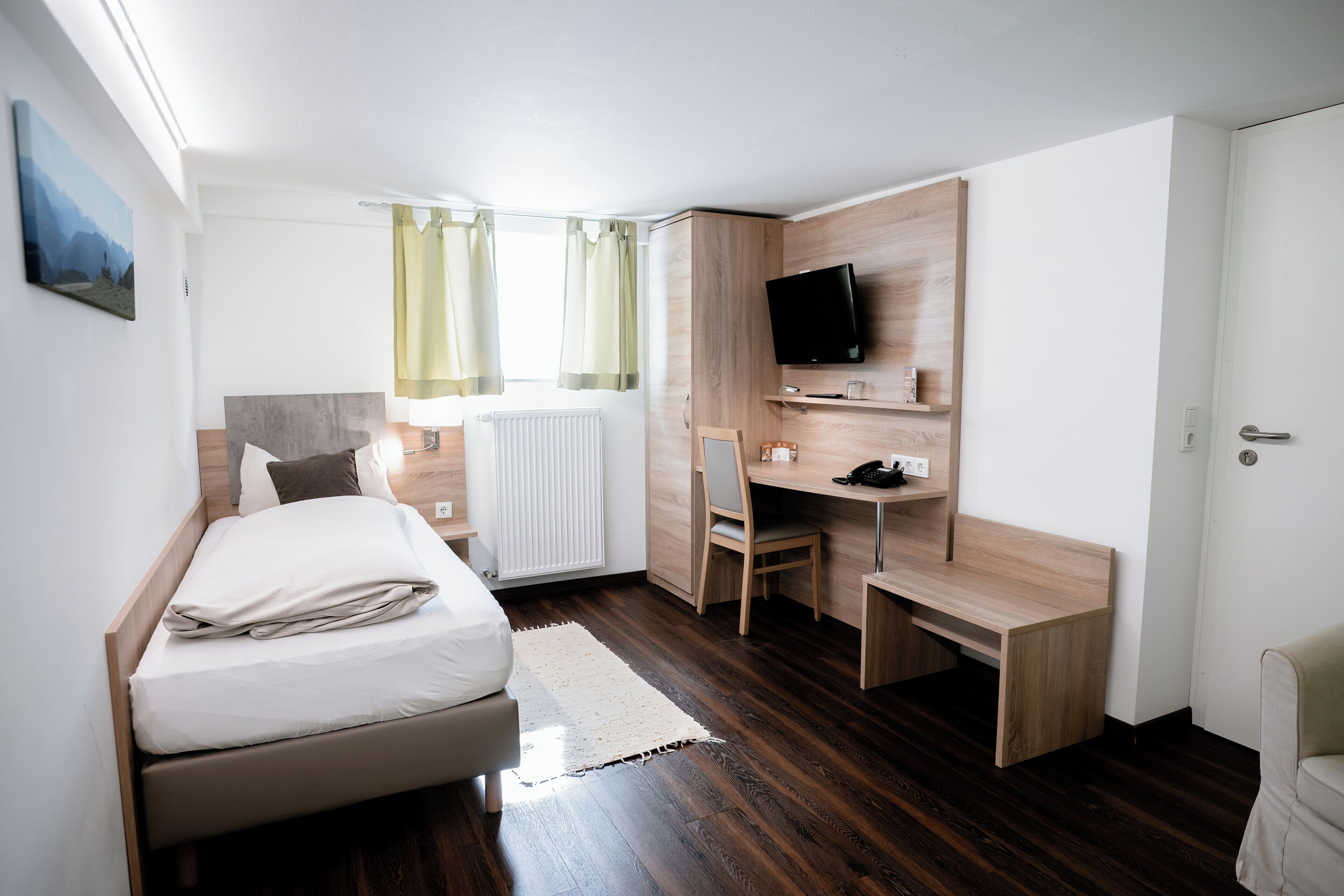 A bedroom with a bed, a desk, a chair, a television, and a window with curtains.