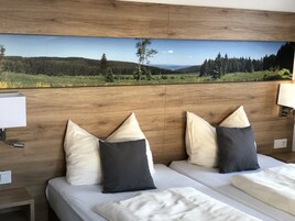 Habitación de hotel con dos camas, cabecero de madera y un cuadro de paisaje grande sobre las camas.
