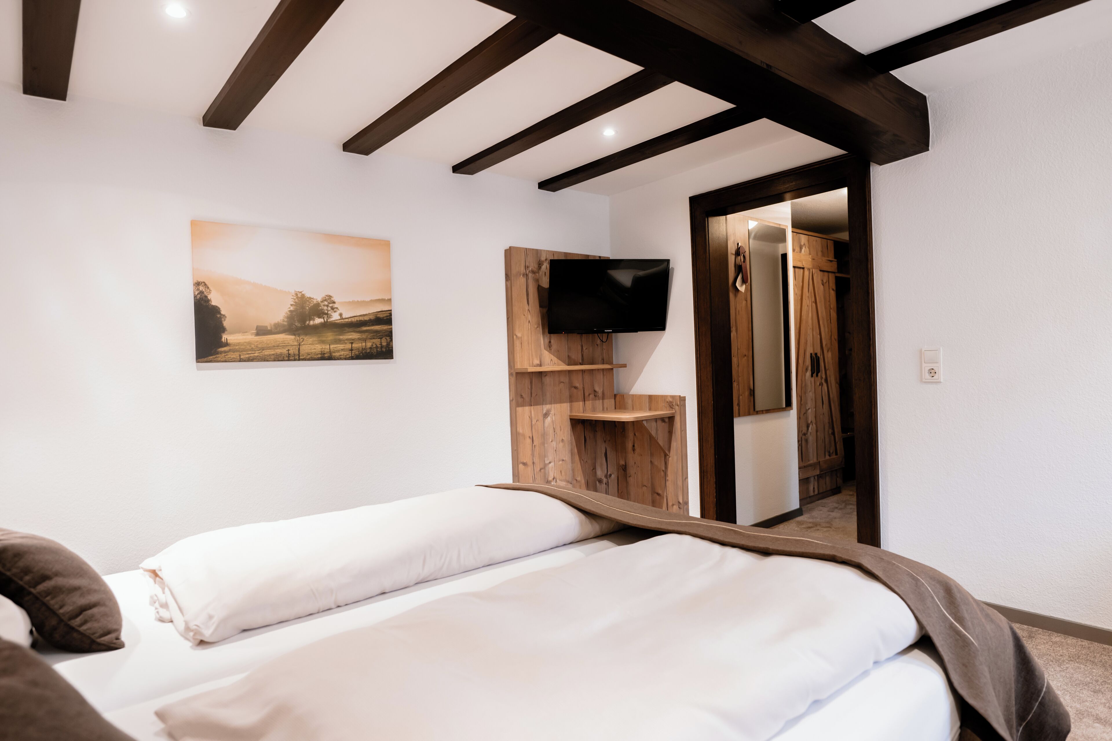 A bedroom with a bed, a wooden TV stand, a painting, and a wardrobe.