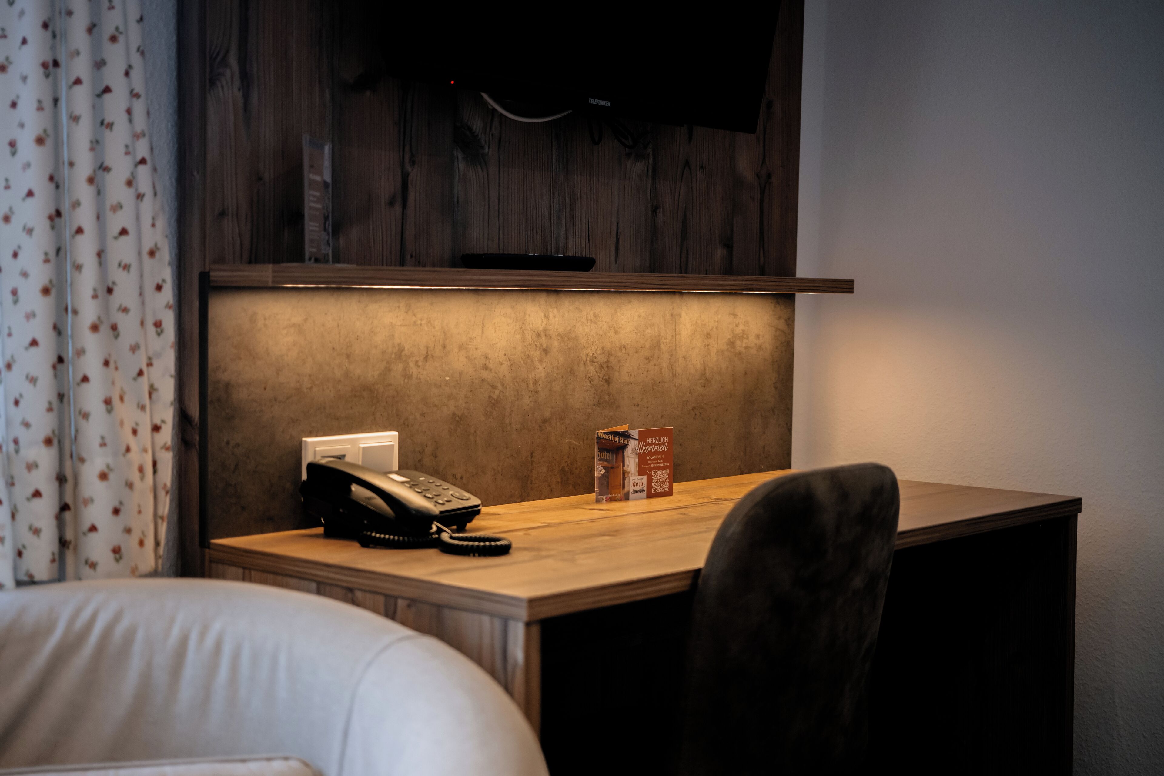 Hotellihuone, jossa on puinen työpöytä, puhelin ja paketti paperisia nenäliinoja.