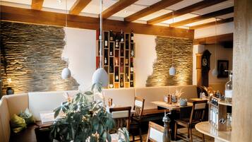Ein gemütliches Restaurant mit Holzbalken, Steinwänden und verschiedenen Sitzgelegenheiten, darunter eine Bank und Tische.