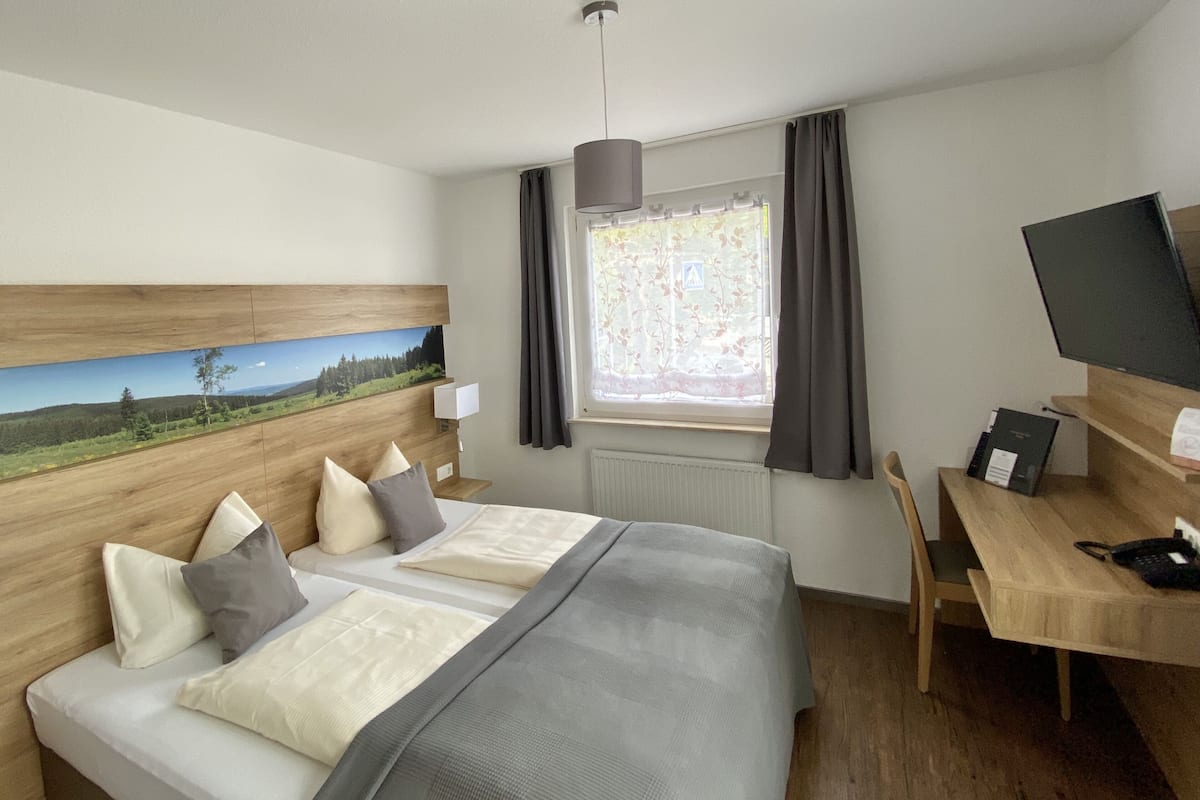 A hotel room with a large bed, a desk, a chair, a TV, and a window with curtains.
