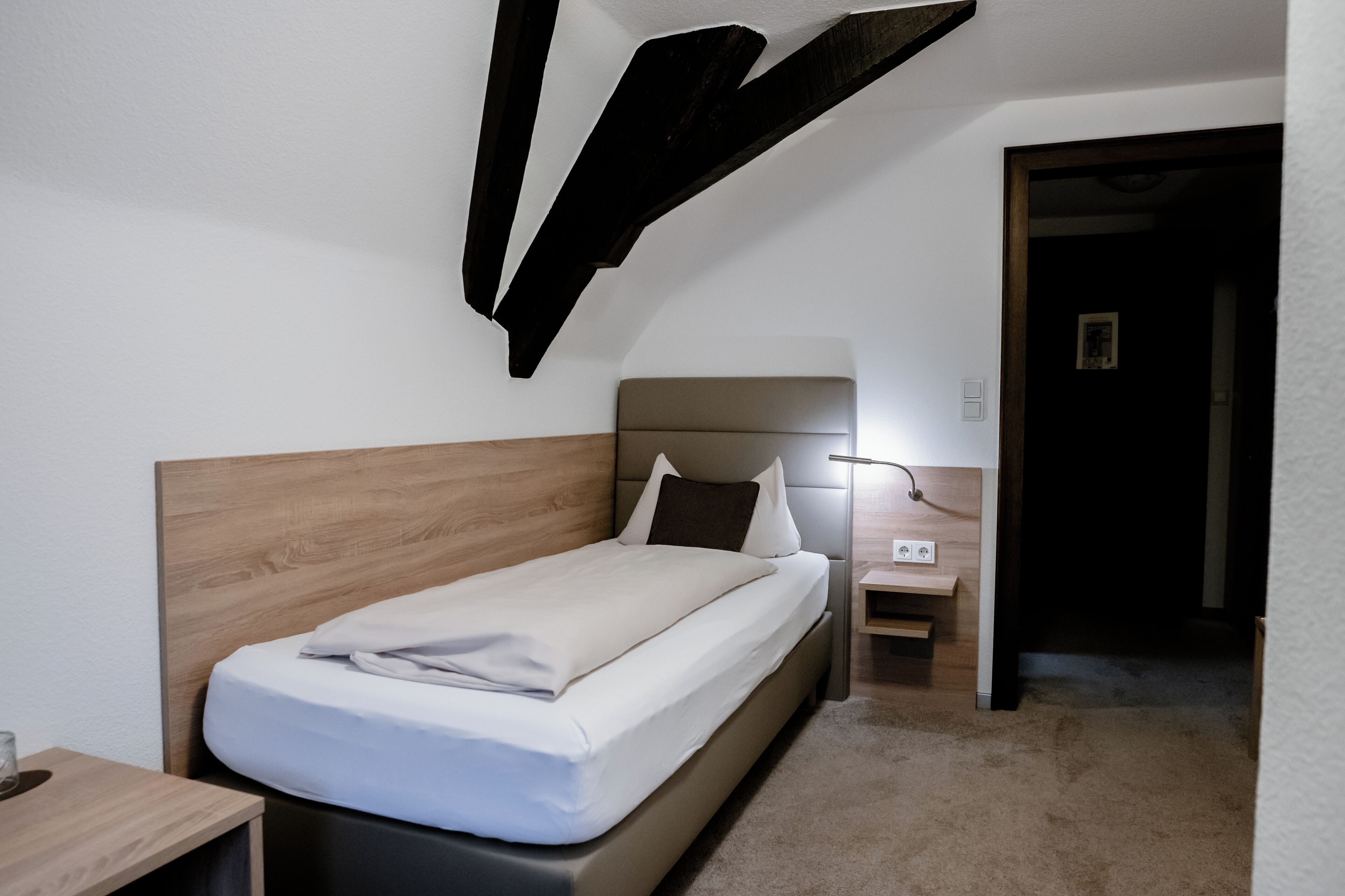 A single bed with a wooden headboard, a bedside table, and a nightstand with a lamp.