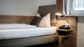 Una cama bien hecha con cabecera de madera, una mesita de noche con lámpara y teléfono.
