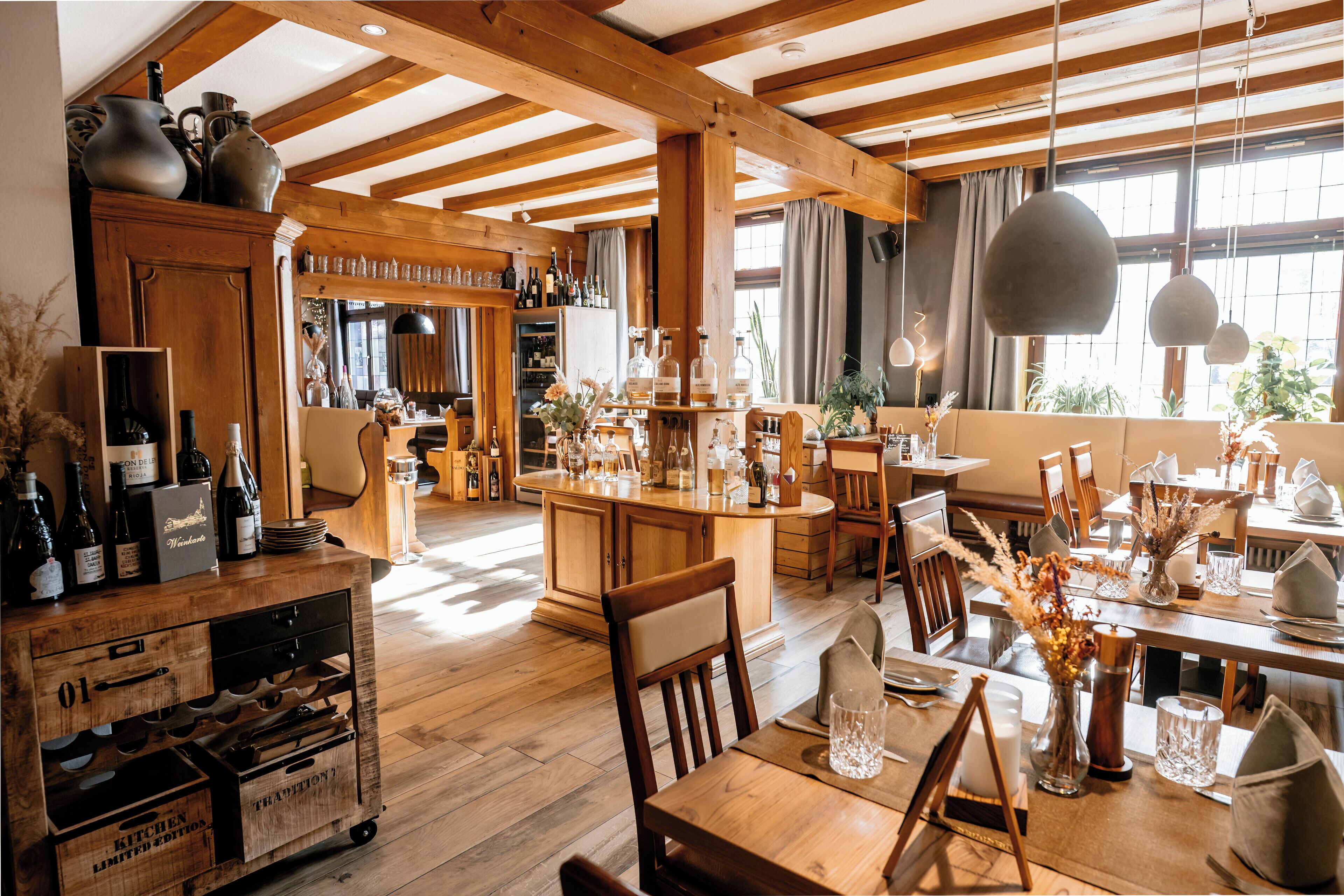 Un intérieur rustique avec des poutres en bois, un coin bar avec des bouteilles et un espace repas avec des chaises et des tables.