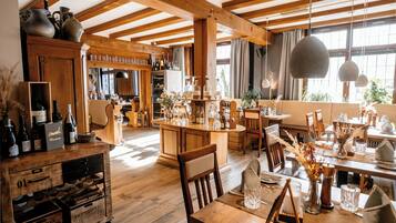 A rustic interior with wooden beams, a bar area with bottles, and a dining space with chairs and tables.