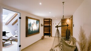 A hallway with a wooden door, a framed picture of a forest, a hanging hammock, and a massage table. - Hotel Gasthof Koch (Daaden)