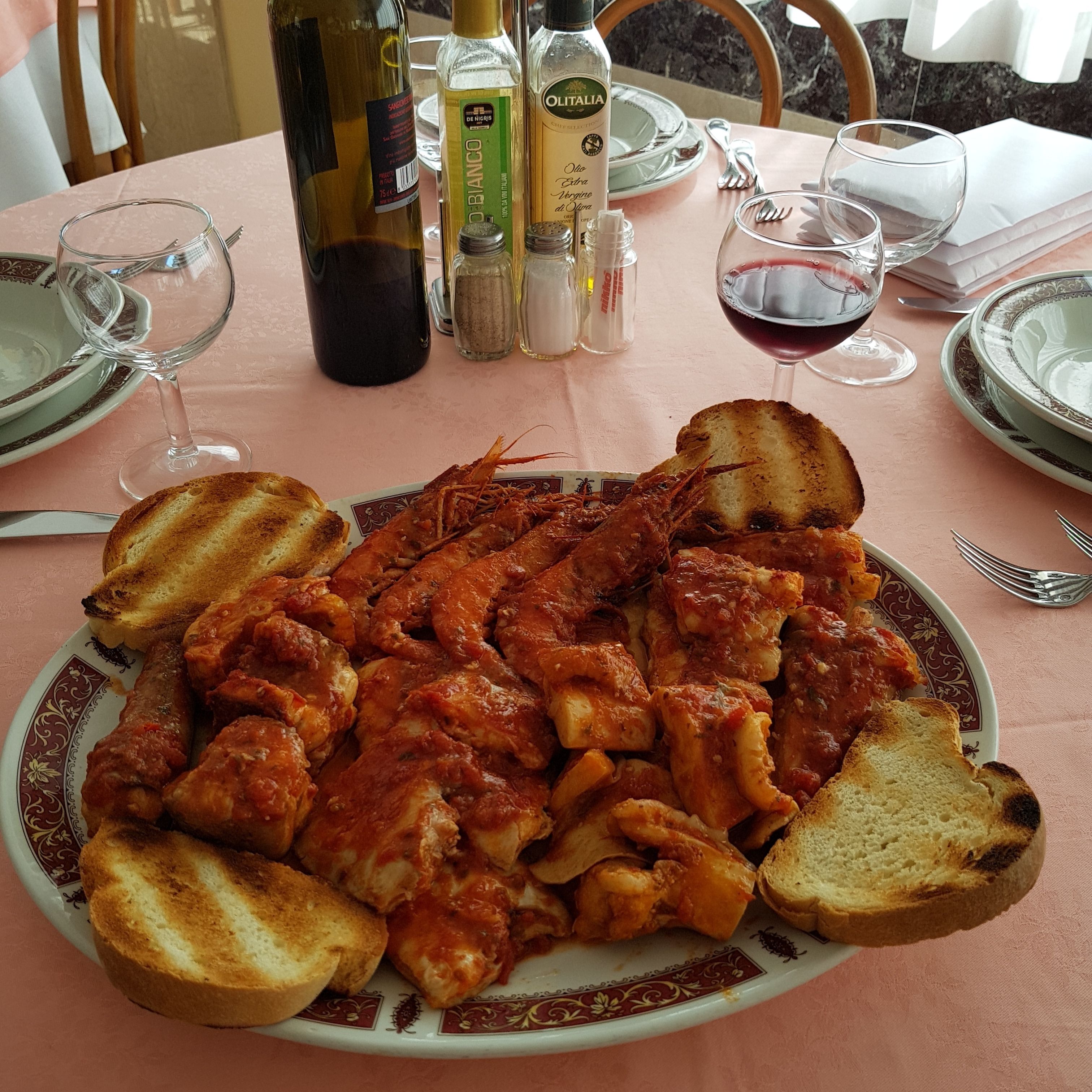A dining table with a plate of food, wine glasses, and bottles of olive oil.