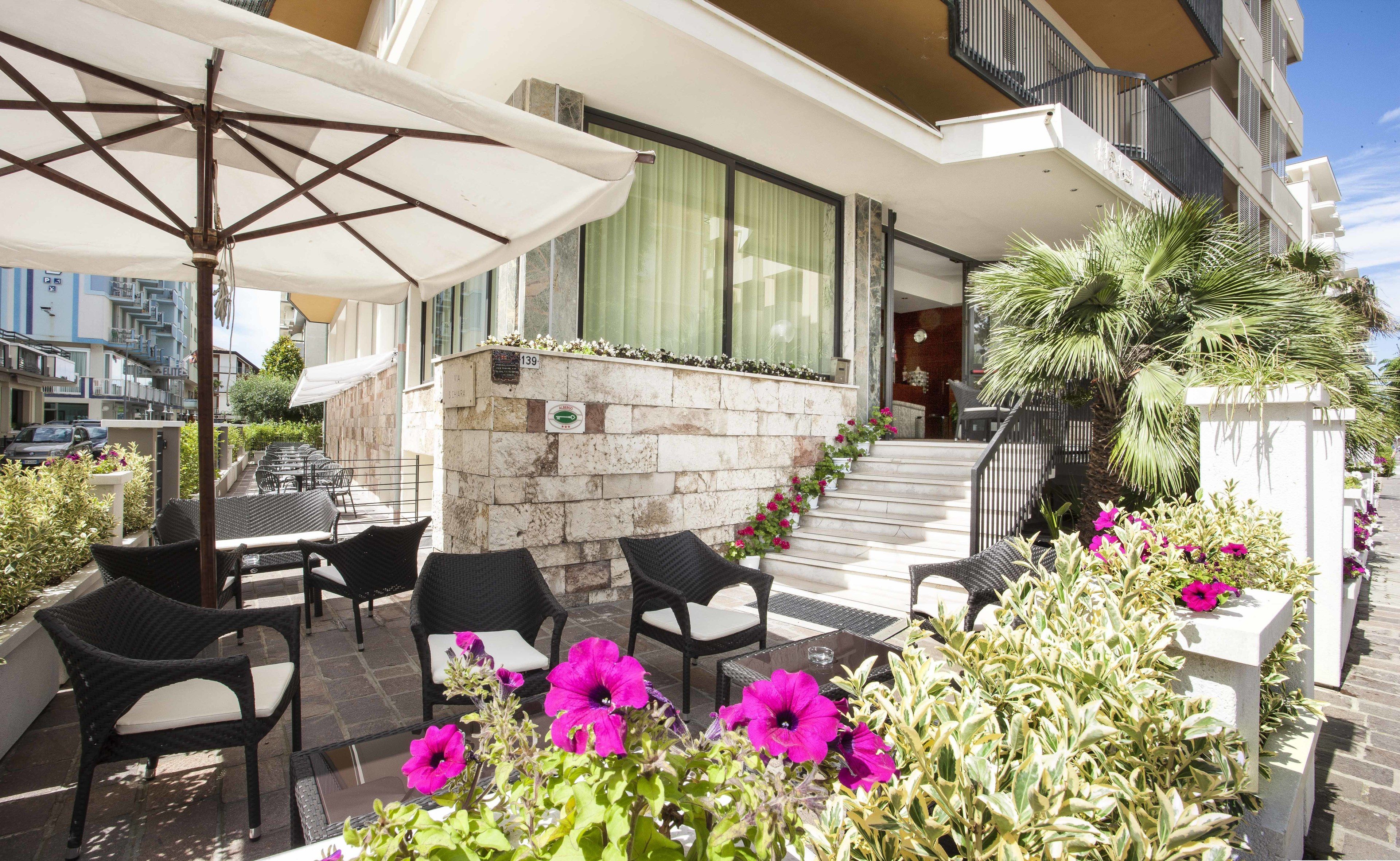 An outdoor seating area with wicker chairs and a table, a stone wall with a plaque, and a staircase leading to a balcony.
