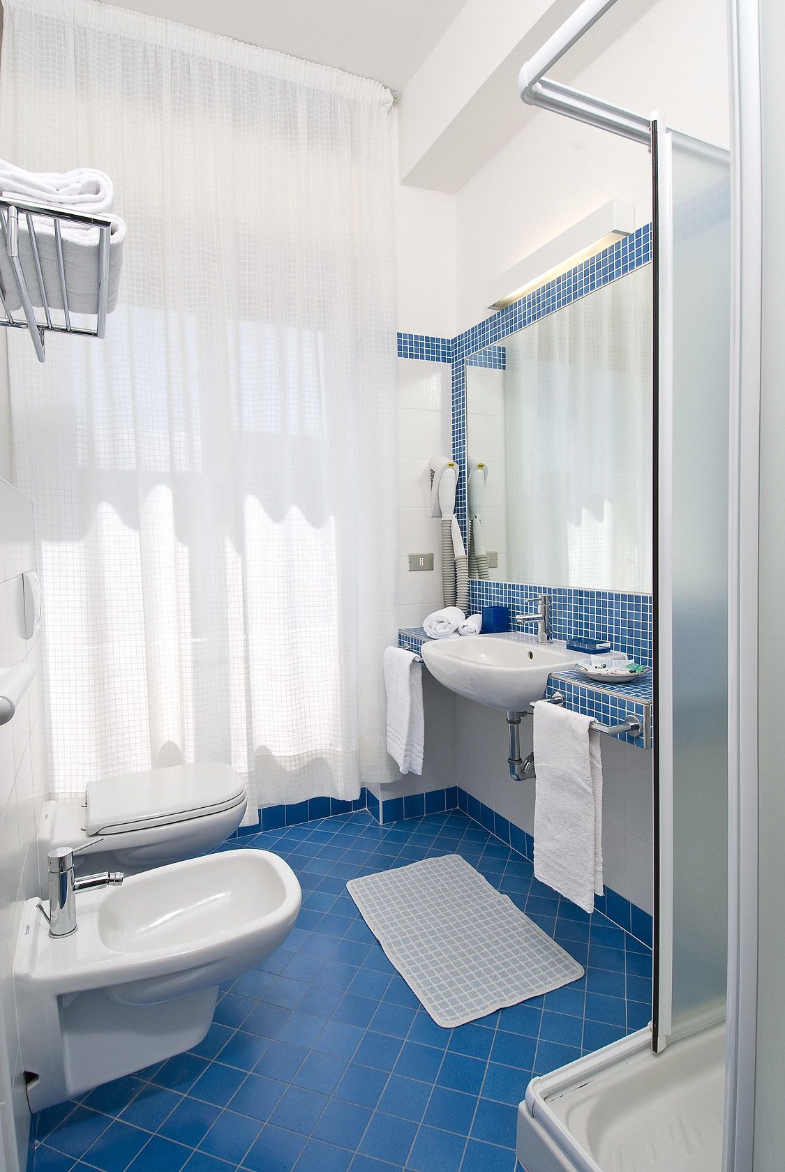 Un baño con inodoro, bidé, lavamanos y ducha.