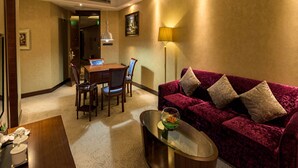 Un salon avec un canapé en velours rouge, une table basse en verre, une table à manger avec des chaises et un tableau accroché au mur.
