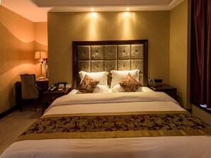 Una habitación de hotel con una cama grande, un cabecero con panel texturizado, una mesita de noche con lámpara y una silla.