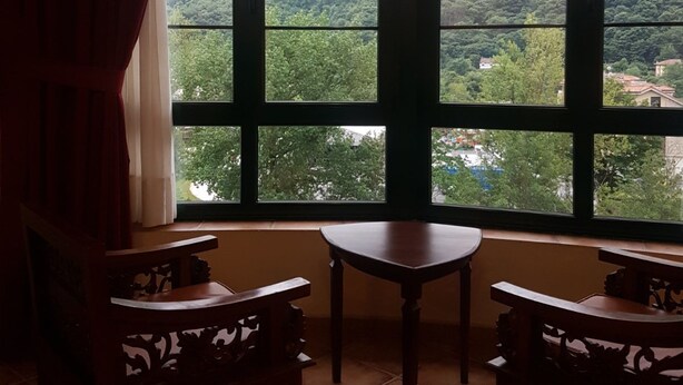 A room with a large window overlooking a mountainous landscape. There are two wooden chairs and a small table in the room. - Apartamentos Villa de Cabrales (Cabrales)
