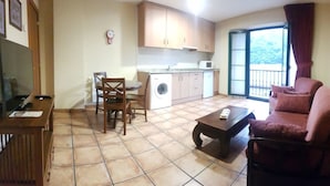 A compact living space with a dining area, a sofa, a coffee table, a washing machine, and a balcony with a view. - Apartamentos Villa de Cabrales (Cabrales)
