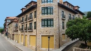 A multi-story building with stone facade and balconies, located on a street with a sidewalk and a lamp post. - Apartamentos Villa de Cabrales (Cabrales)