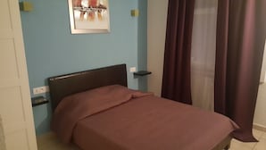 Een slaapkamer met een bed, nachtkastje, een wandplank en een schilderij.