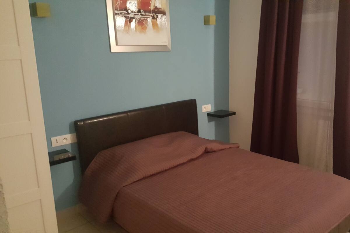 A bedroom with a bed, a nightstand, a wall-mounted shelf, and a painting.