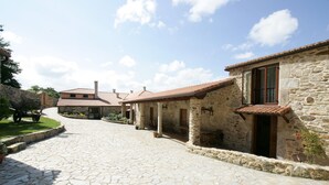 A stone pathway leading to a rustic building with a tiled roof, stone walls, and a small balcony. - Casa da Botica (A Estrada)