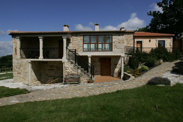 A stone house with a porch, a staircase, and a small garden. - Casa da Botica (A Estrada)