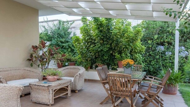Un patio couvert aménagé avec des meubles en osier et une table en bois.