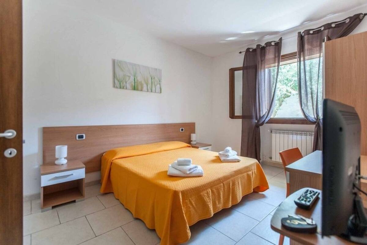 Ein Hotelzimmer mit Bett, Schreibtisch mit Computer, Fernseher und einem Fenster mit Vorhängen.