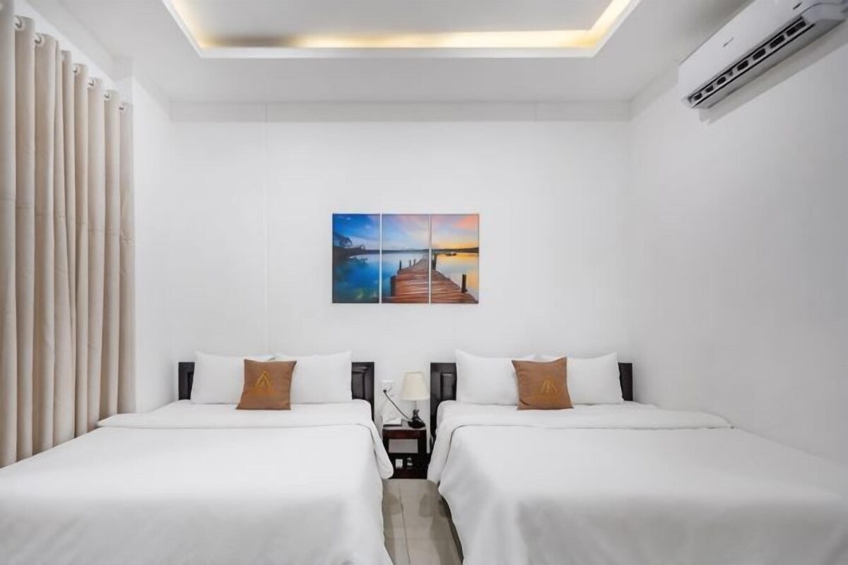 Habitació d'hotel amb dos llits, una tauleta de nit amb una làmpada, un quadre a la paret i un aparell d'aire condicionat.