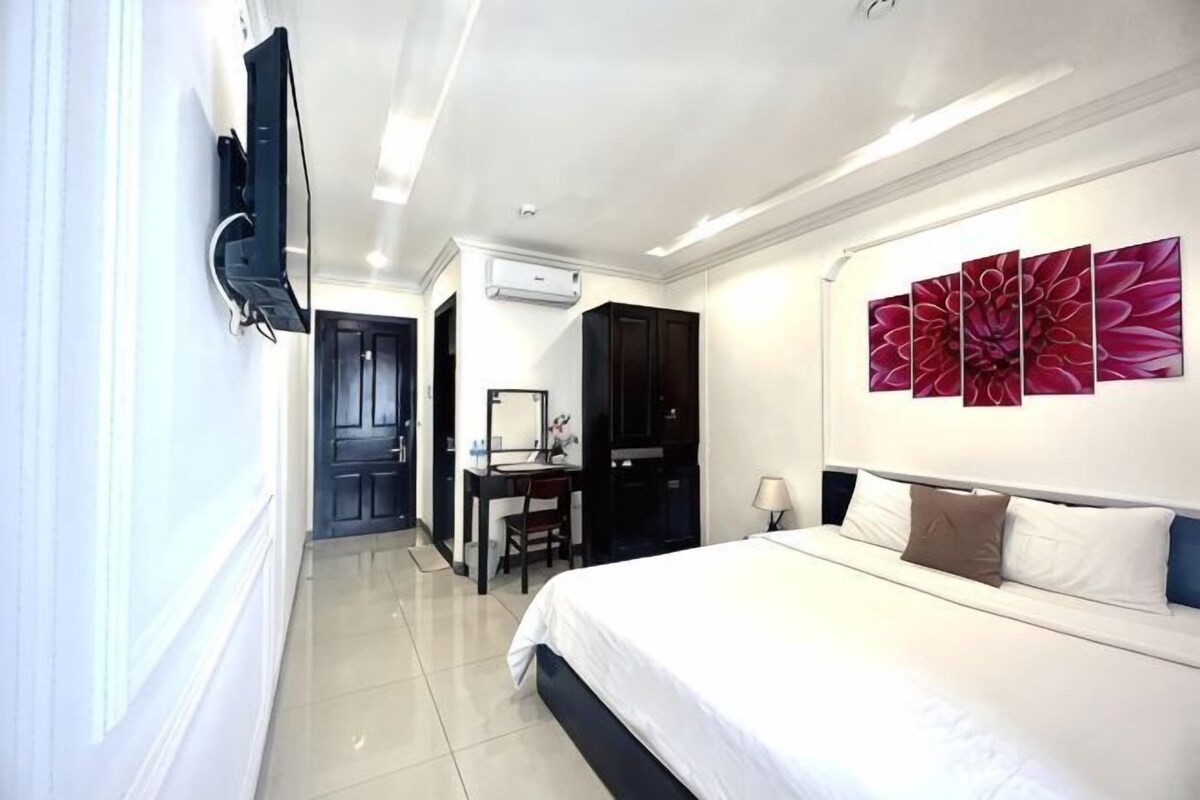 Habitación de hotel con cama, escritorio, silla, televisión y un cuadro grande con motivos florales en la pared.