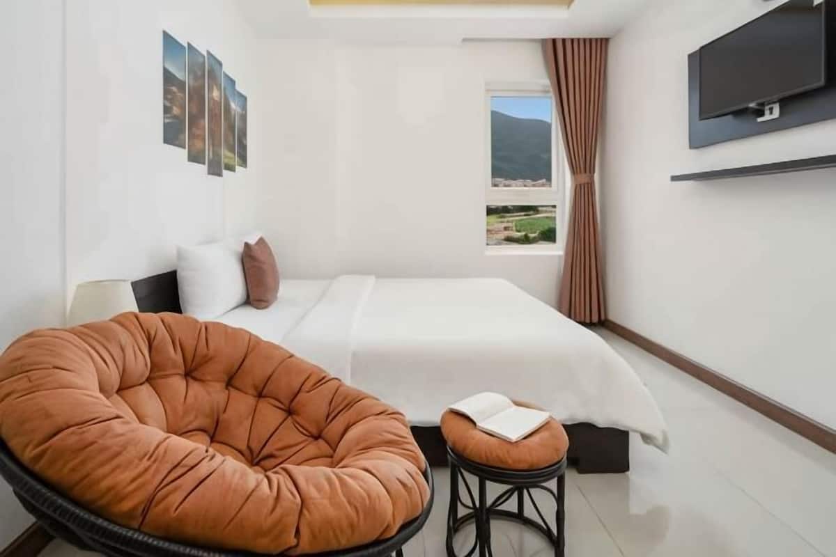 A bedroom with a bed, a large window, a television, and a chair.
