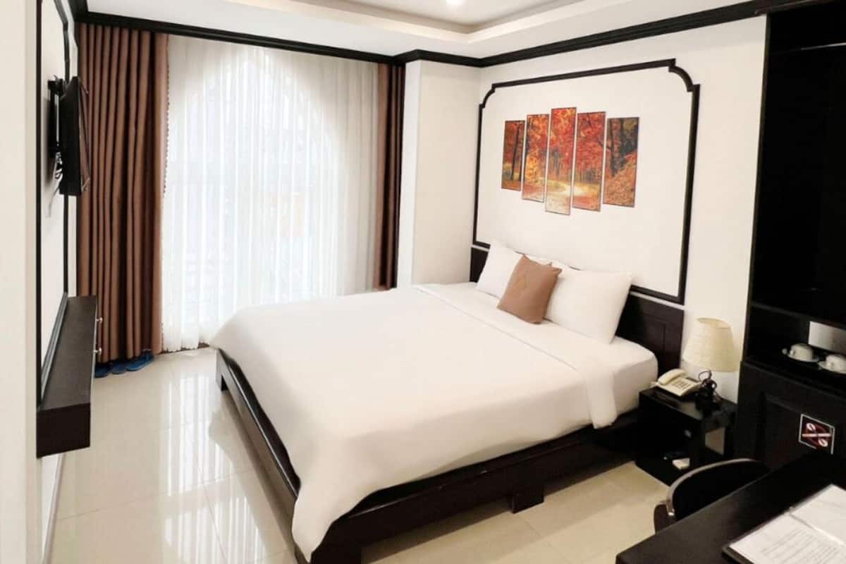A hotel room with a large bed, a desk with a lamp, and a television.