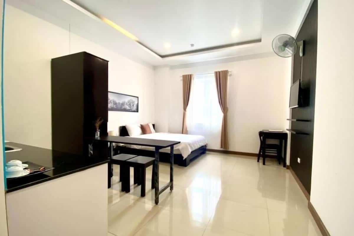 A modern hotel room with a bed, a desk, a chair, a TV, and a wardrobe.