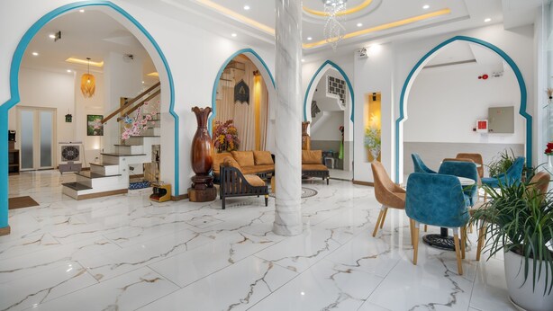 A spacious lobby with marble flooring, blue archways, a central column, and a staircase leading to upper floors. - Phuong Dong Hotel & Apartment (Quy Nhon Nam)