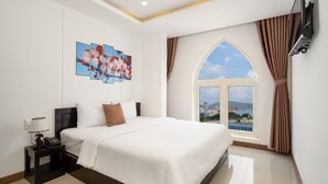 A hotel room with a large bed, a nightstand with a lamp, a phone, and a flat-screen TV mounted on the wall. - Phuong Dong Hotel & Apartment (Quy Nhon Nam)