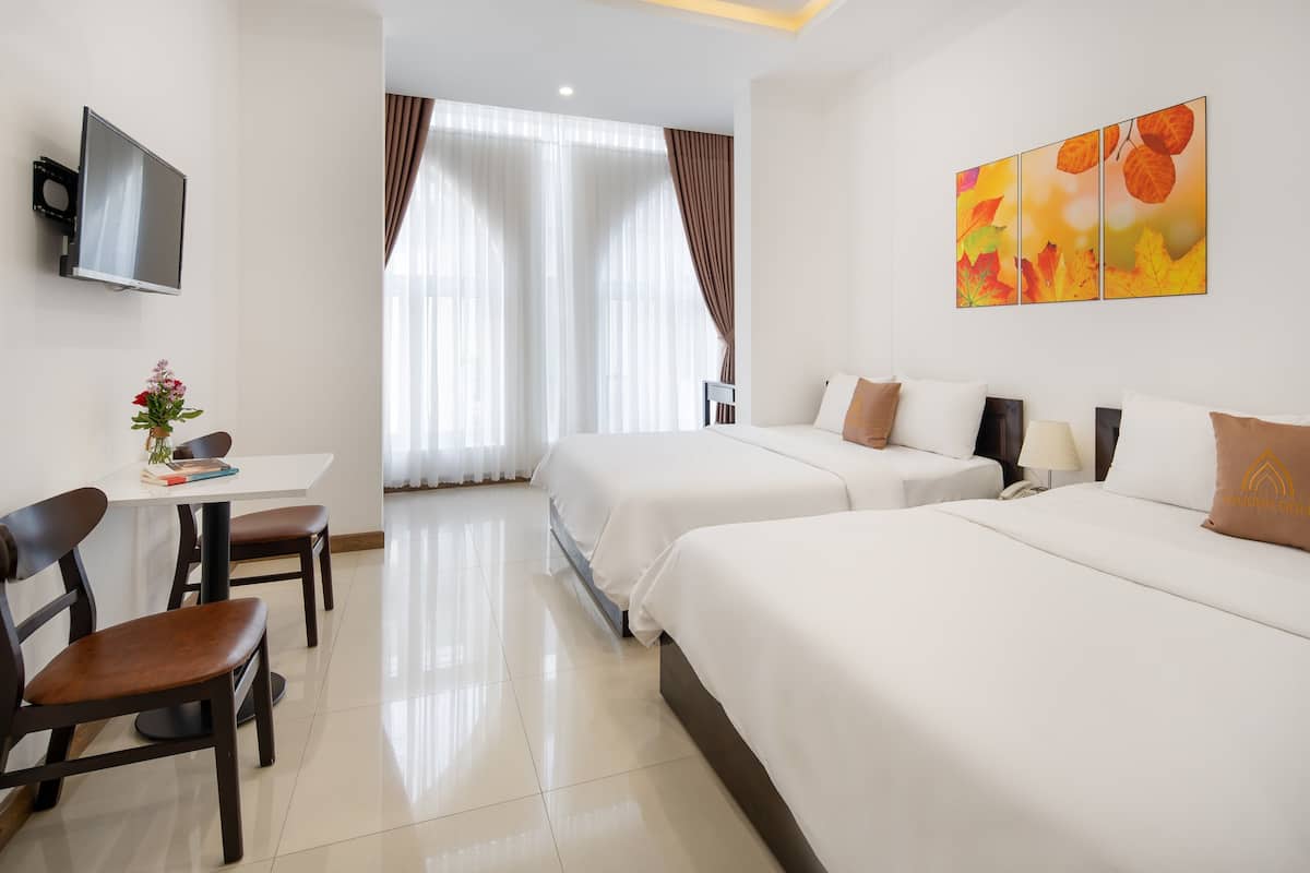 A hotel room with two beds, a desk with chairs, a TV, and a painting on the wall.