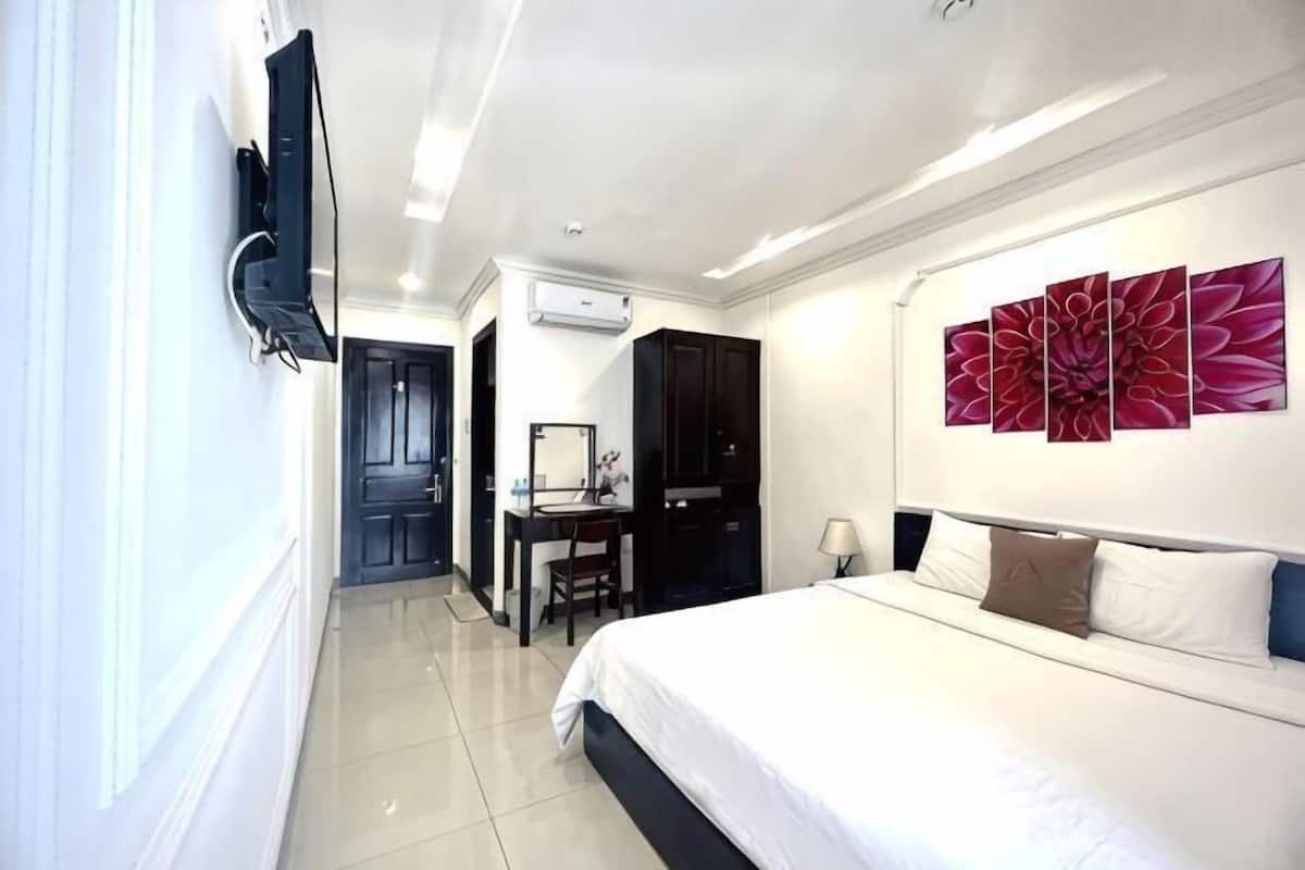 A hotel room with a bed, a desk, a chair, a TV, and a large floral artwork on the wall.