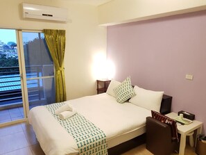 Habitación de hotel con cama, mesita de noche, lámpara, ventana con cortinas y aire acondicionado.