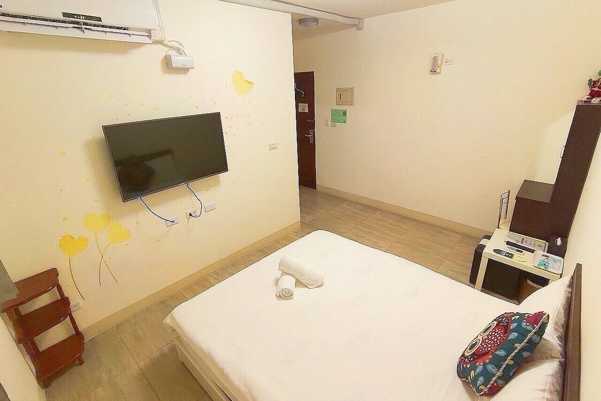 A hotel room with a bed, a TV mounted on the wall, a desk with a chair, and a small table.