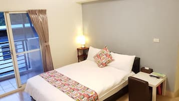 A hotel room with a bed, a bedside table, a lamp, a window with curtains, and a view of the outside.