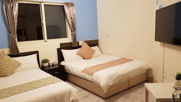 Une chambre avec deux lits, une fenêtre avec des rideaux, un téléviseur à écran plat et une petite table sur laquelle est posée une plante.