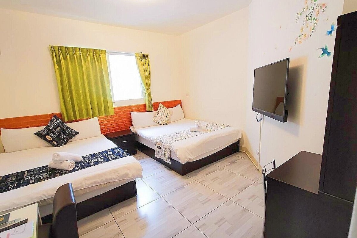 A hotel room with two beds, a TV, and a desk.