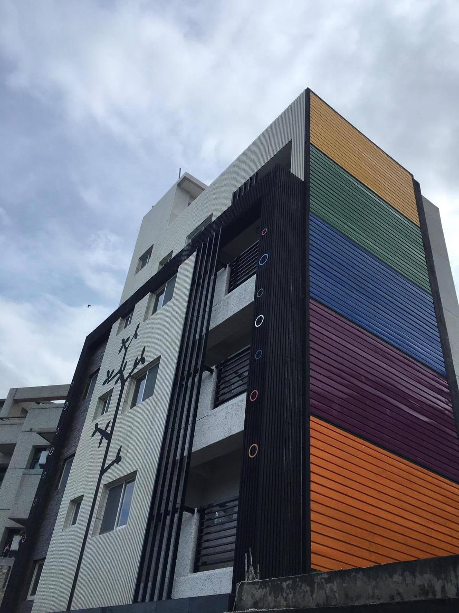 A multi-story building with a modern architectural design, featuring a combination of white and dark panels, and a section with colorful horizontal stripes.