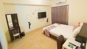 Une chambre d’hôtel équipée d’un lit, d’un bureau, d’une chaise, d’un miroir, d’une télévision et d’un élément décoratif mural.