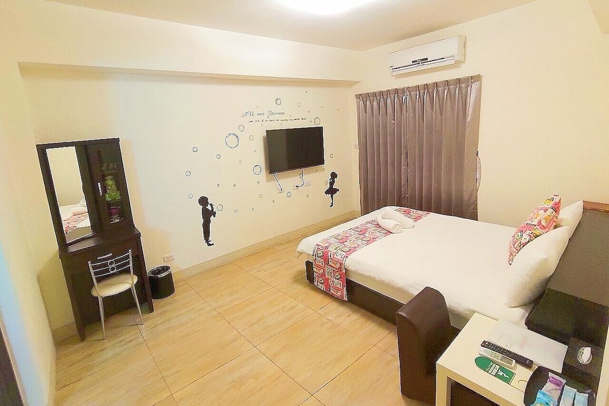 A hotel room with a bed, a desk, a chair, a mirror, a television, and a wall decoration.