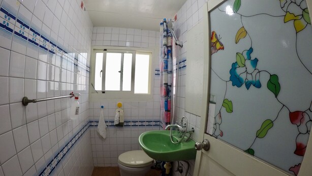 Un bagno piccolo con pareti rivestite di piastrelle bianche, un lavandino verde, un water e una finestra.