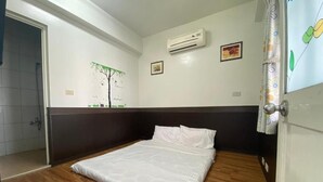 Una stanza con un letto, pavimento in legno, condizionatore d'aria a muro e cabina doccia.