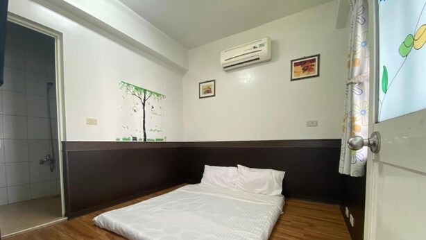 A room with a bed, wooden flooring, a wall-mounted air conditioner, and a shower area. - Danke Hostel (Liuqiu)