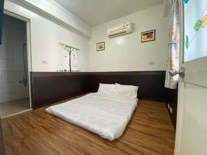 A room with a bed, wooden flooring, a wall-mounted air conditioner, and a shower area. - Danke Hostel (Liuqiu)